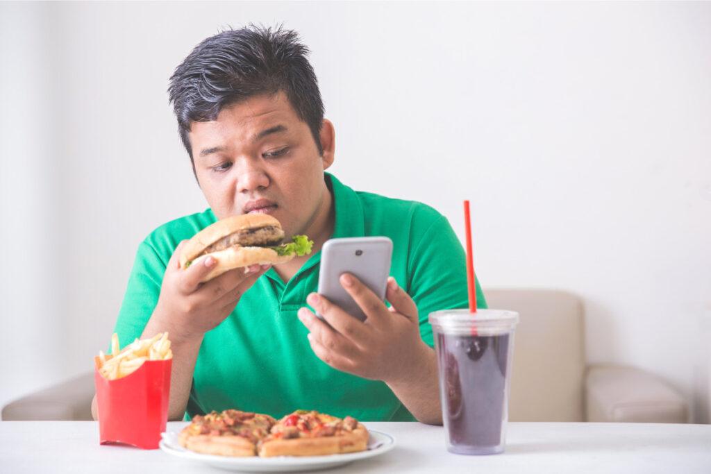 スマホを見ながらジャンクフードを食べる男性